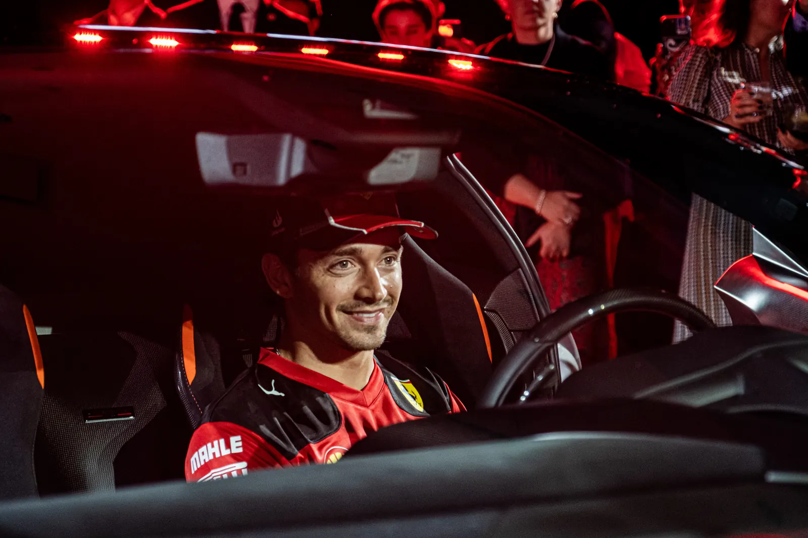 Charles Leclerc smiling from the driver's seat of a Ferrari as guests look on at the Ferrari of Austin reveal event